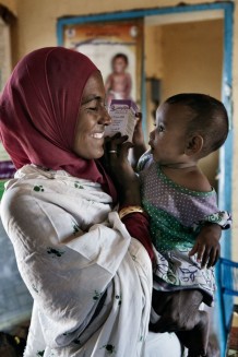 Amany Dowd, cleaner of the health center, taking drugs for her daughter Dalia Aboadem, 1 year old, sick with flue, by medical assistant Ahmed Hassan Ahmed. Drugs are provided by Italian Cooperation. Ardalhager health centre, Girba locality, Kassala State. Sudan 2015