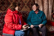 Tetiana, 47, a local community worker, left, and Maria, a beneficiary, during a home visit. Maria is 67, widowed for 10 years, and lives alone. "We had lots of fruit trees," she says. Hence the name of the village: "sad" means fruit garden, thus "fruit garden village." Tetiana is also the director of the kindergarten. But since the kindergarten is closed, and her husband has been away at war since 2014, she helps out by cooking for the many soldiers stationed in the area. Her work as a community worker makes her feel useful. Sadove, Kharkiv Region. Ukraine, 2026